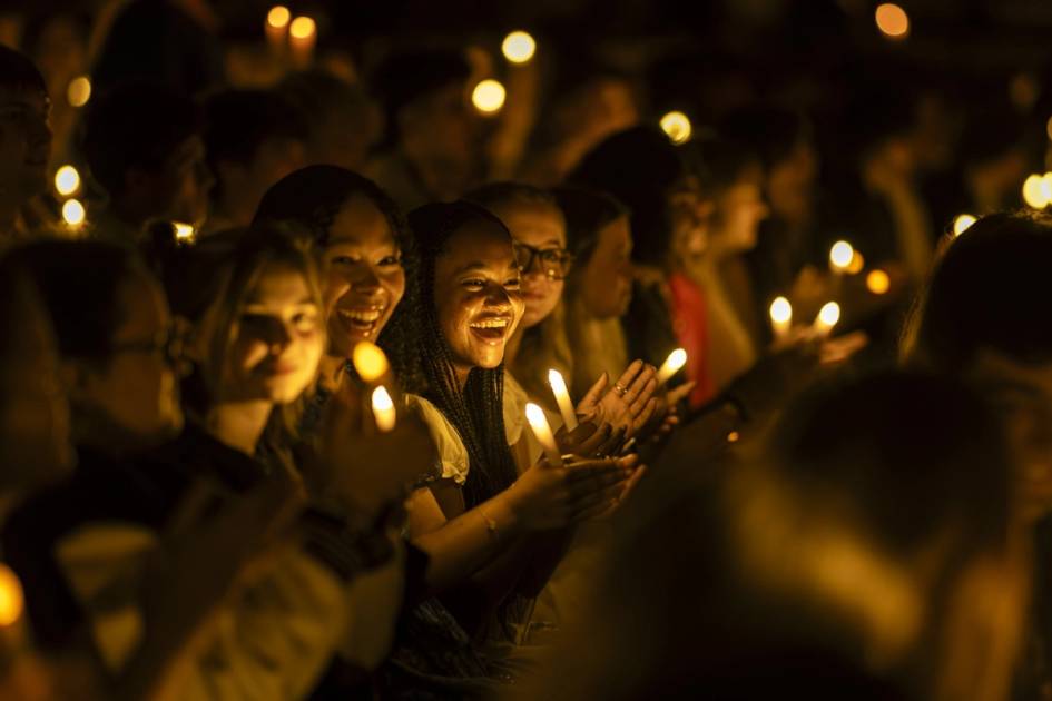 Students with candles sitting together at night, smiling at the camera