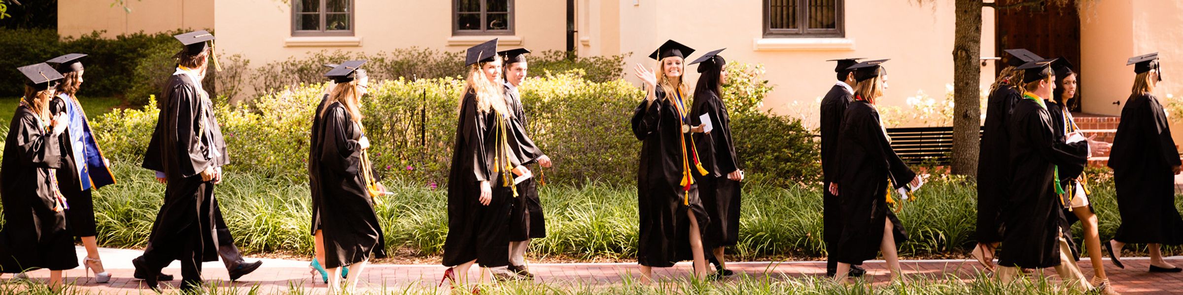 A line of graduates in caps and gowns walk to a commencement ceremony.