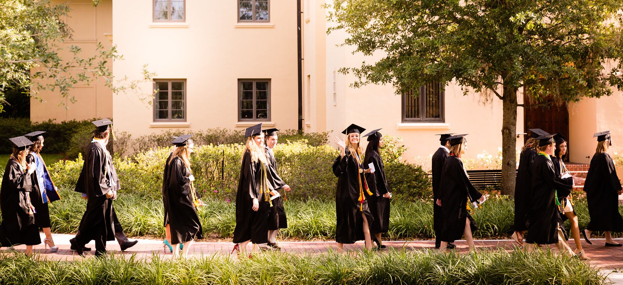 A line of graduates in caps and gowns walk to a commencement ceremony.