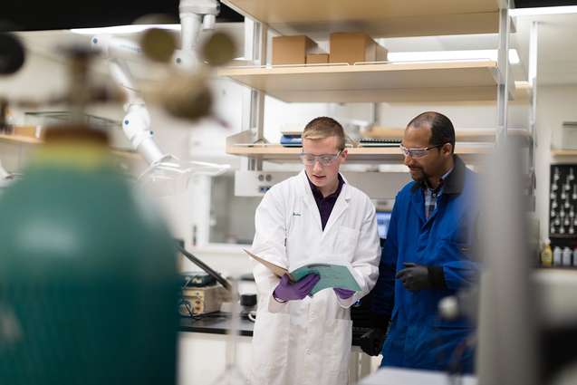 A chemistry college professor is mentoring his student in a chemistry lab as they look at research together.