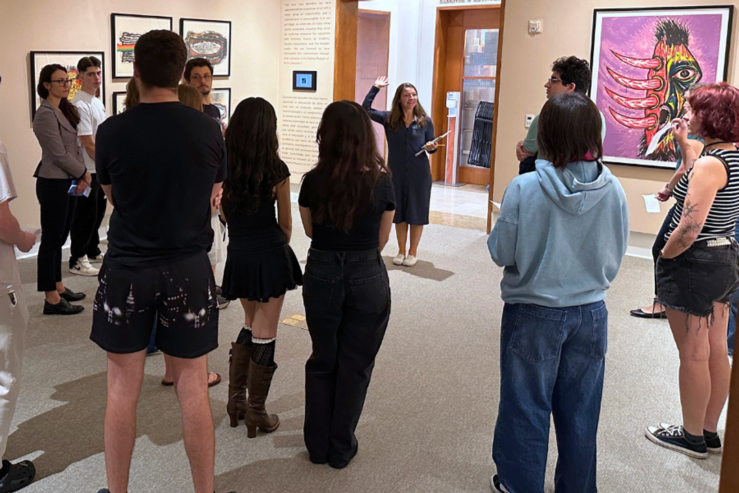Students surrounds man holding works of art in a gallery