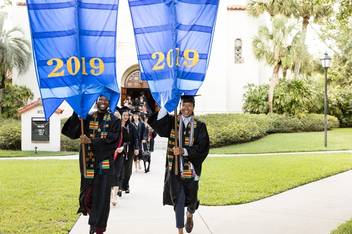 Students in commencement attire carry banners which say 2019 on them.