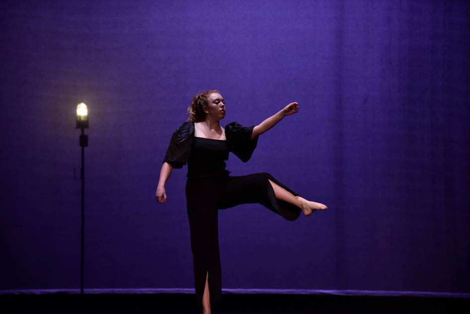 A single dancer next to a ghostlight on an empty stage.