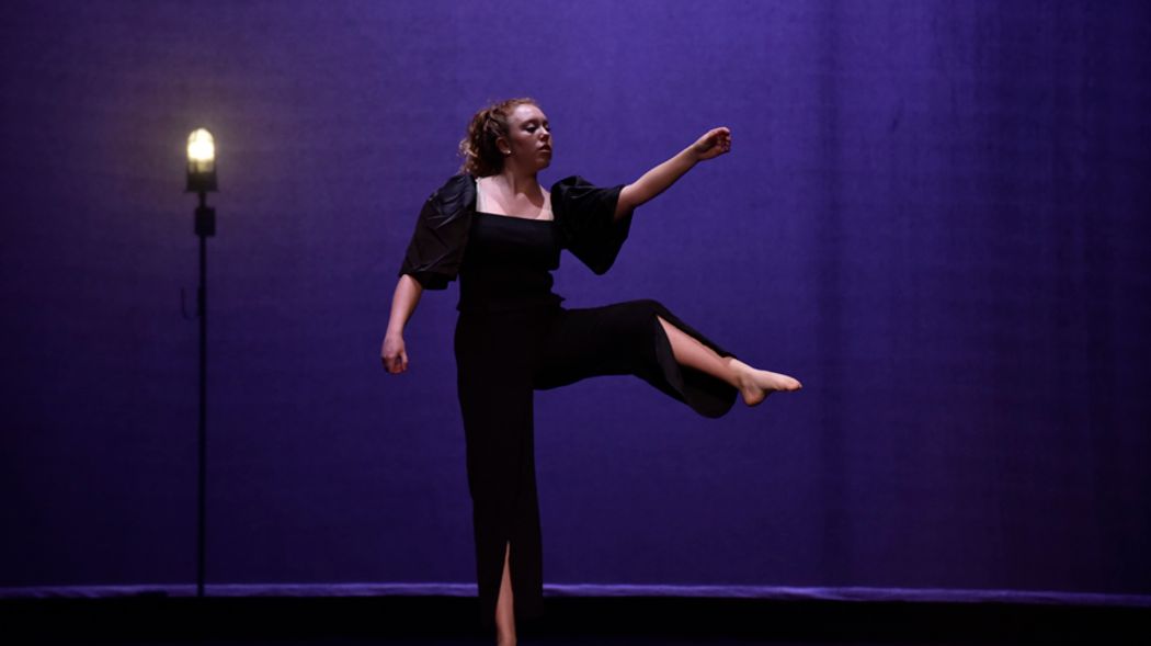 A single dancer next to a ghostlight on an empty stage.