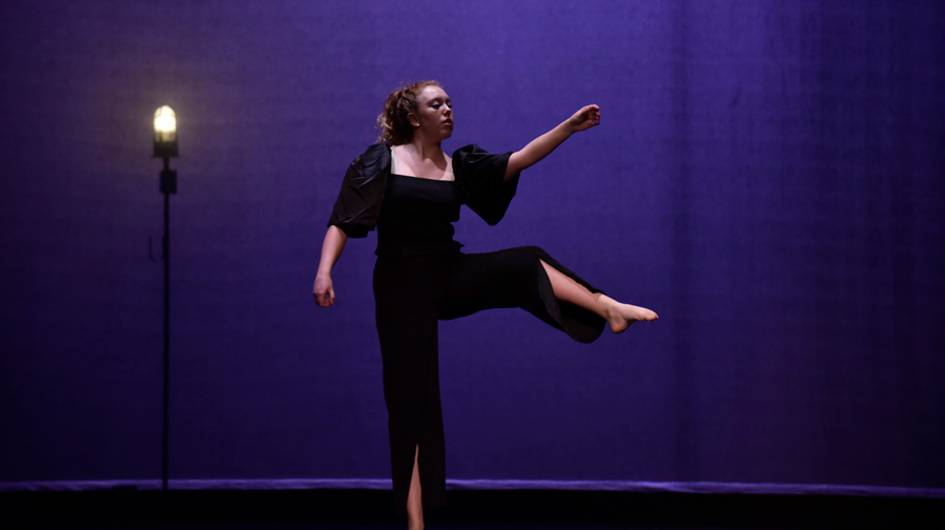 A single dancer next to a ghostlight on an empty stage.