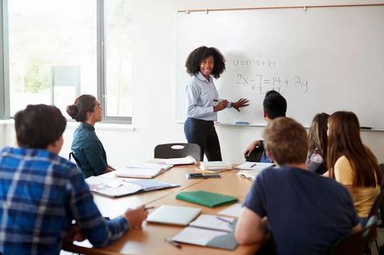 A high school math teacher works through a math problem on a whiteboard.