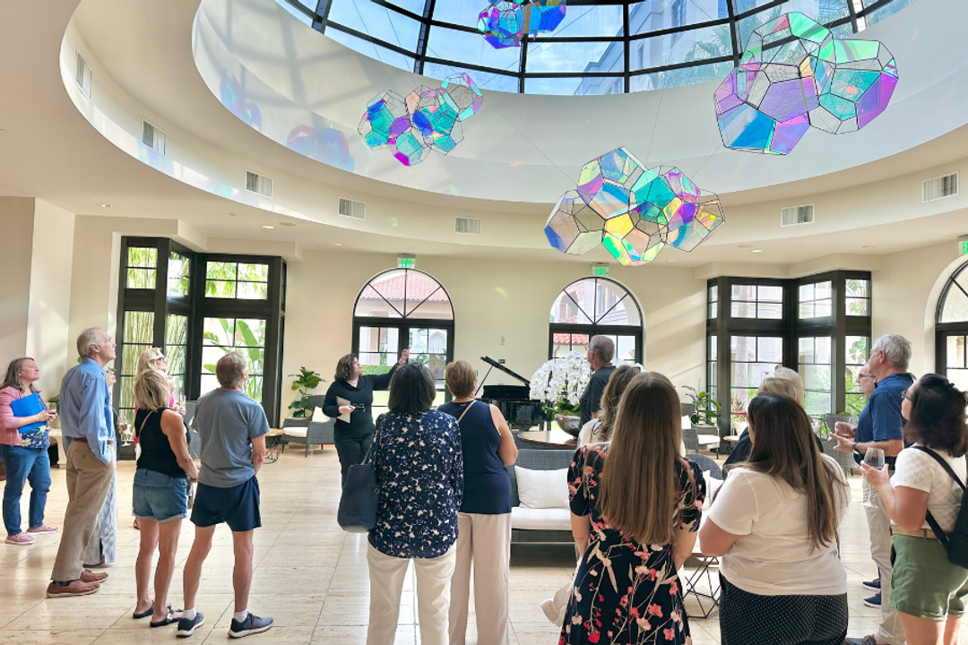 People gather in an atrium looking up at a glass colorful sculpture