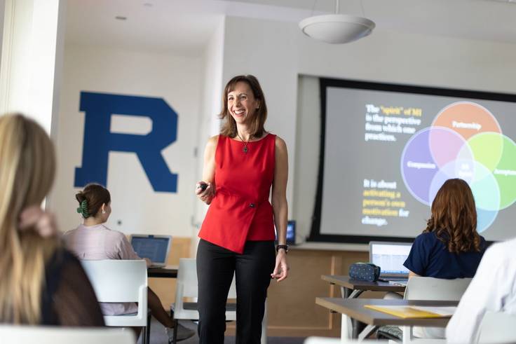 A Rollins professor smiles while standing in her classroom.