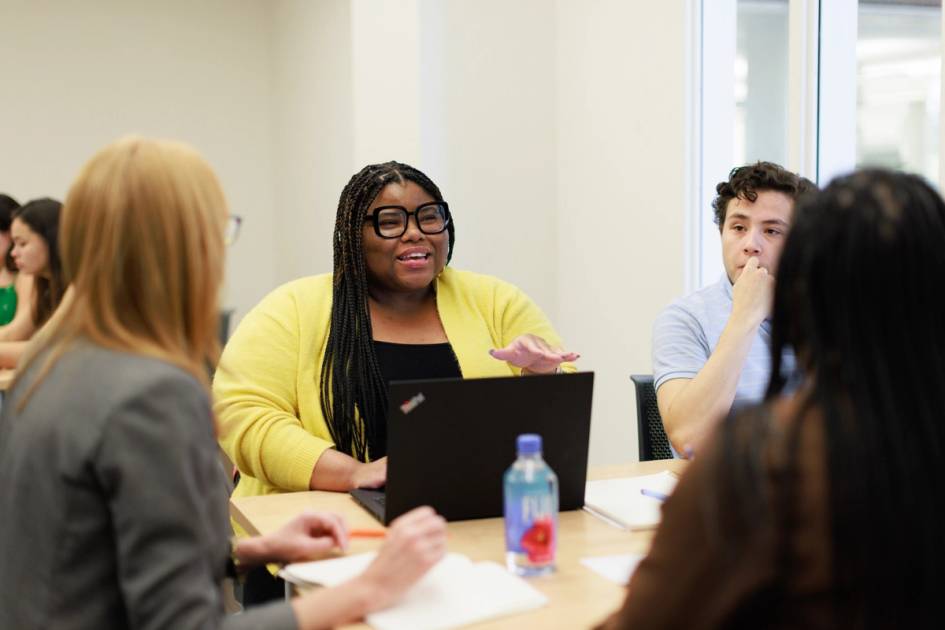 A graduate communication student discusses a project with her professor and a small group of classmates.