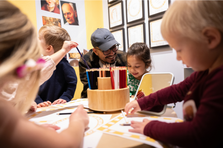 Children and adult drawing together at a colorful art activity table.
