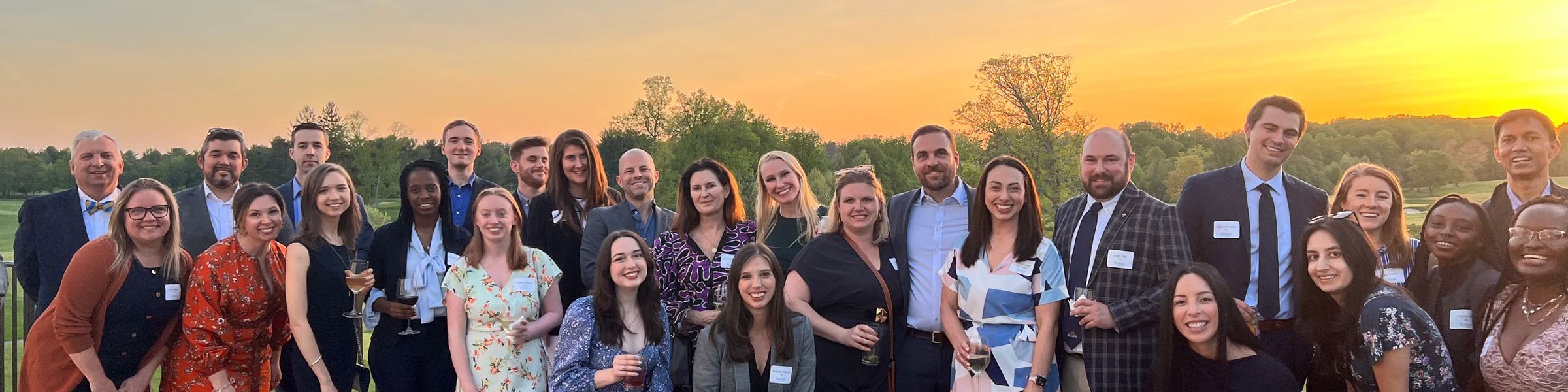 Many alumni standing together in front of a sunset. 