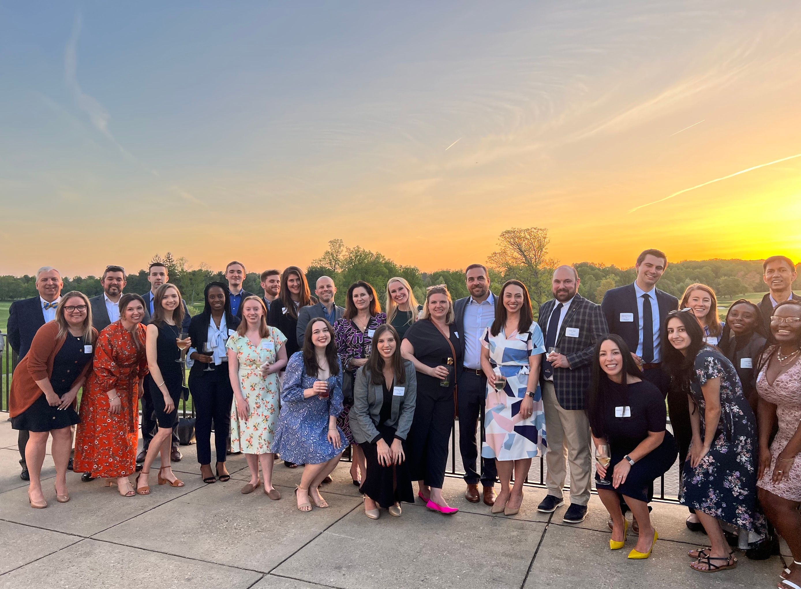 Many alumni standing together in front of a sunset. 