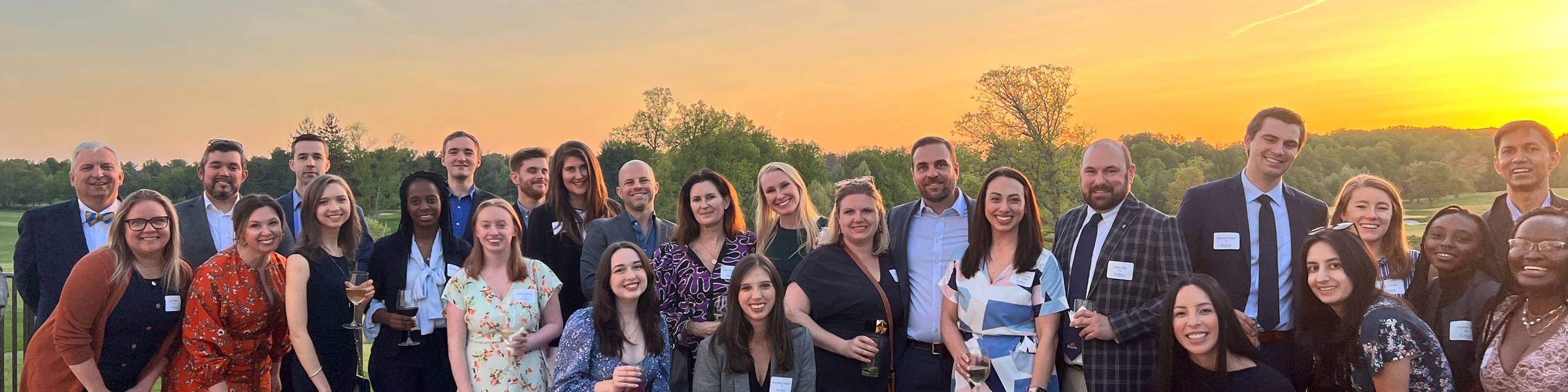 Many alumni standing together in front of a sunset.