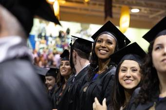A female graduate smiles at her family in the crowd during a commencement ceremony.