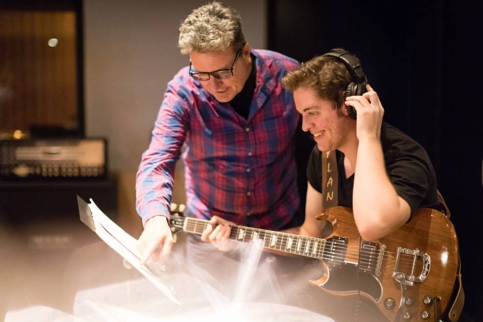 Rollins professor guides a student with a guitar.