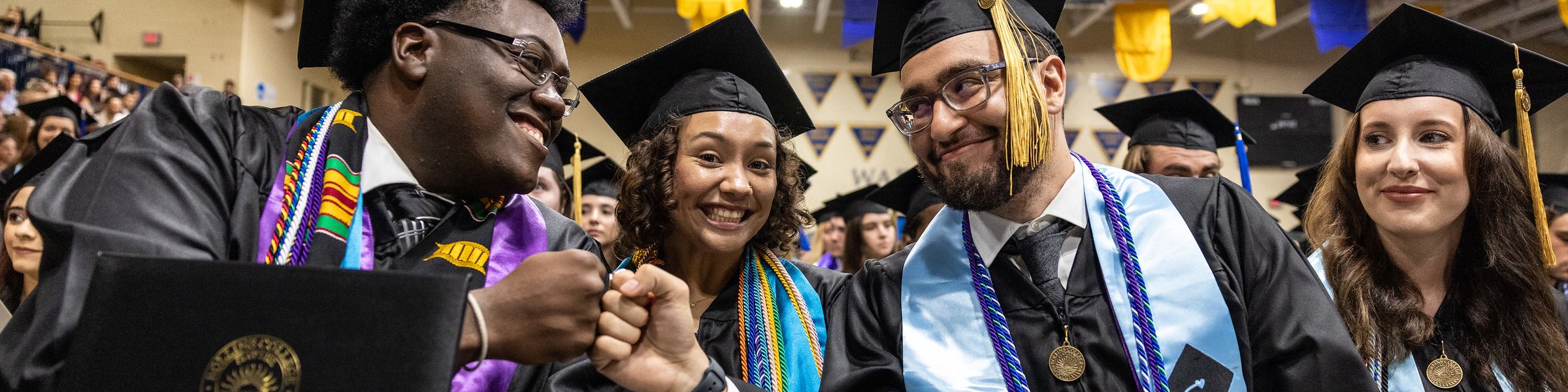 Students in graduation robes, fist-bumping and smiling.