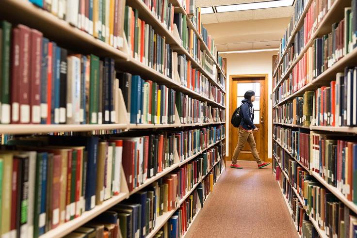 A student walks through the library surrounded by books