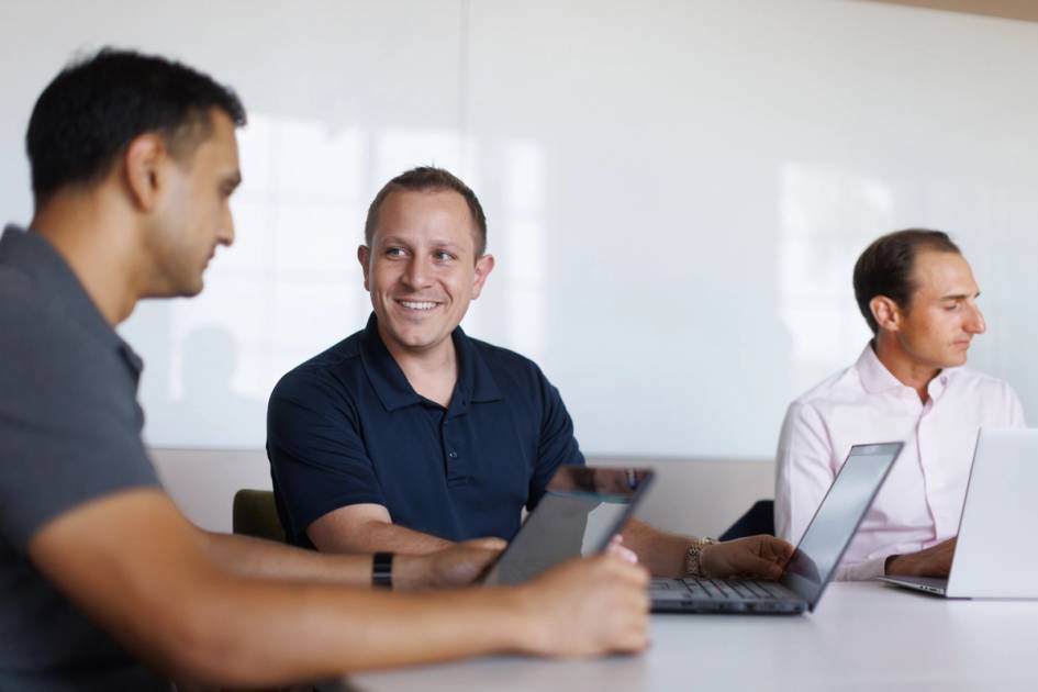 Colleagues collaborating around a conference table with laptops and a tablet.