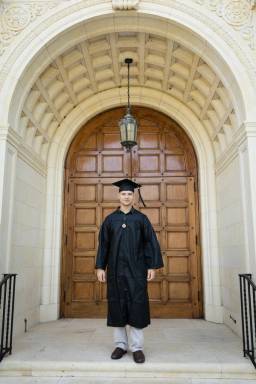 A college graduate poses in cap and gown in front of 91’ Knowles Memorial Chapel.