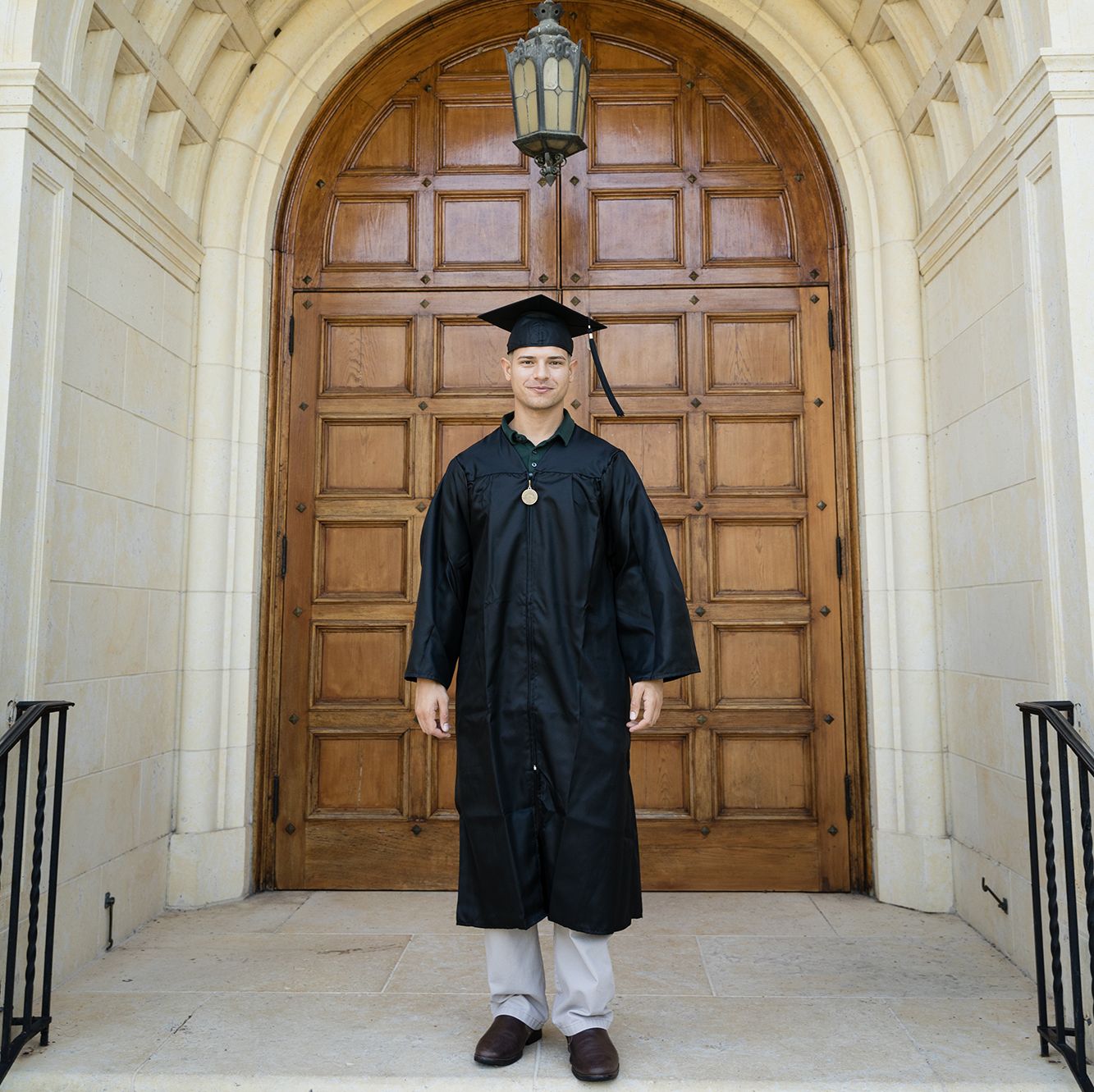 A college graduate poses in cap and gown in front of Rollins’ Knowles Memorial Chapel.