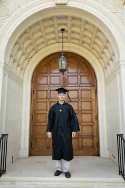A college graduate poses in cap and gown in front of Rollins’ Knowles Memorial Chapel.