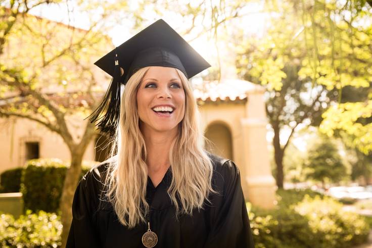 An adult college student wears a cap and gown at a commencement ceremony.