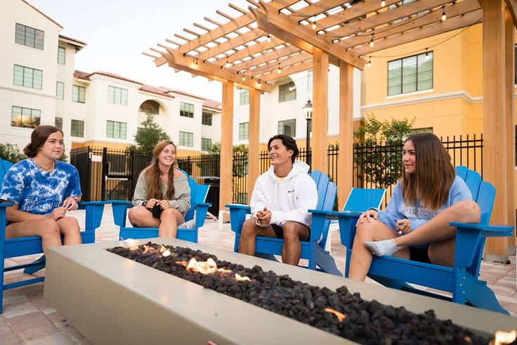 A group of students hang out by an outdoor firepit.
