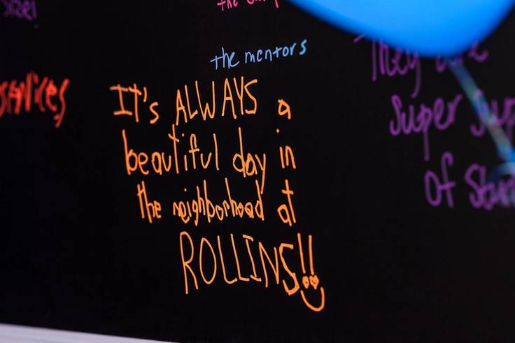 Orange writing on a black chalkboard that says it's always a beautiful day in the neighborhood at Rollins.
