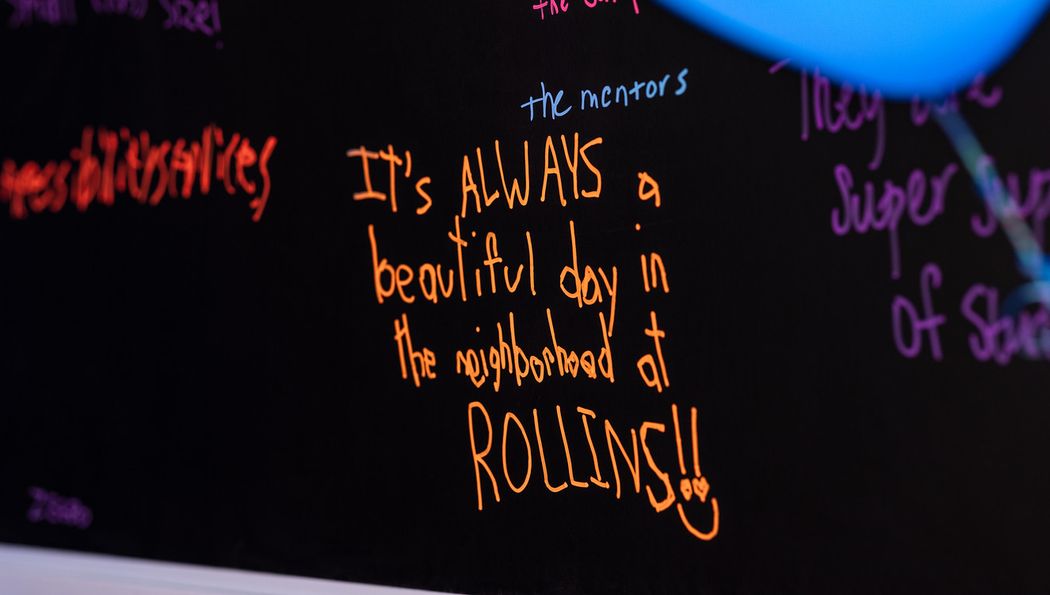 Orange writing on a black chalkboard that says it's always a beautiful day in the neighborhood at Rollins.