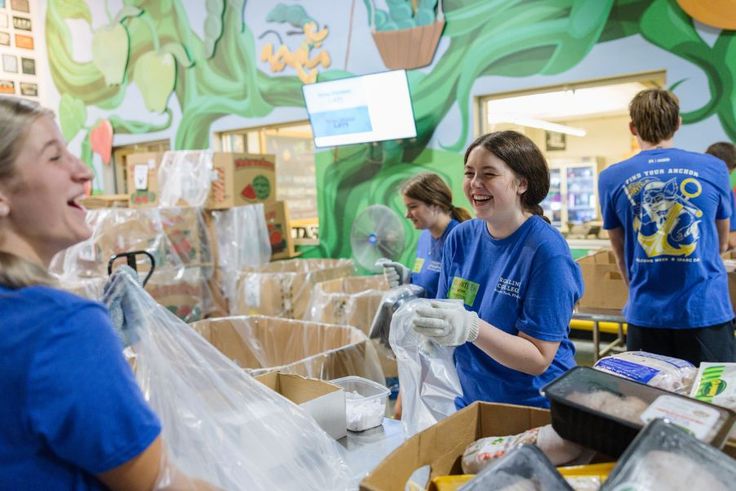 Rollins student volunteers in blue SPARC Day shirts laughing while sorting food at donation center