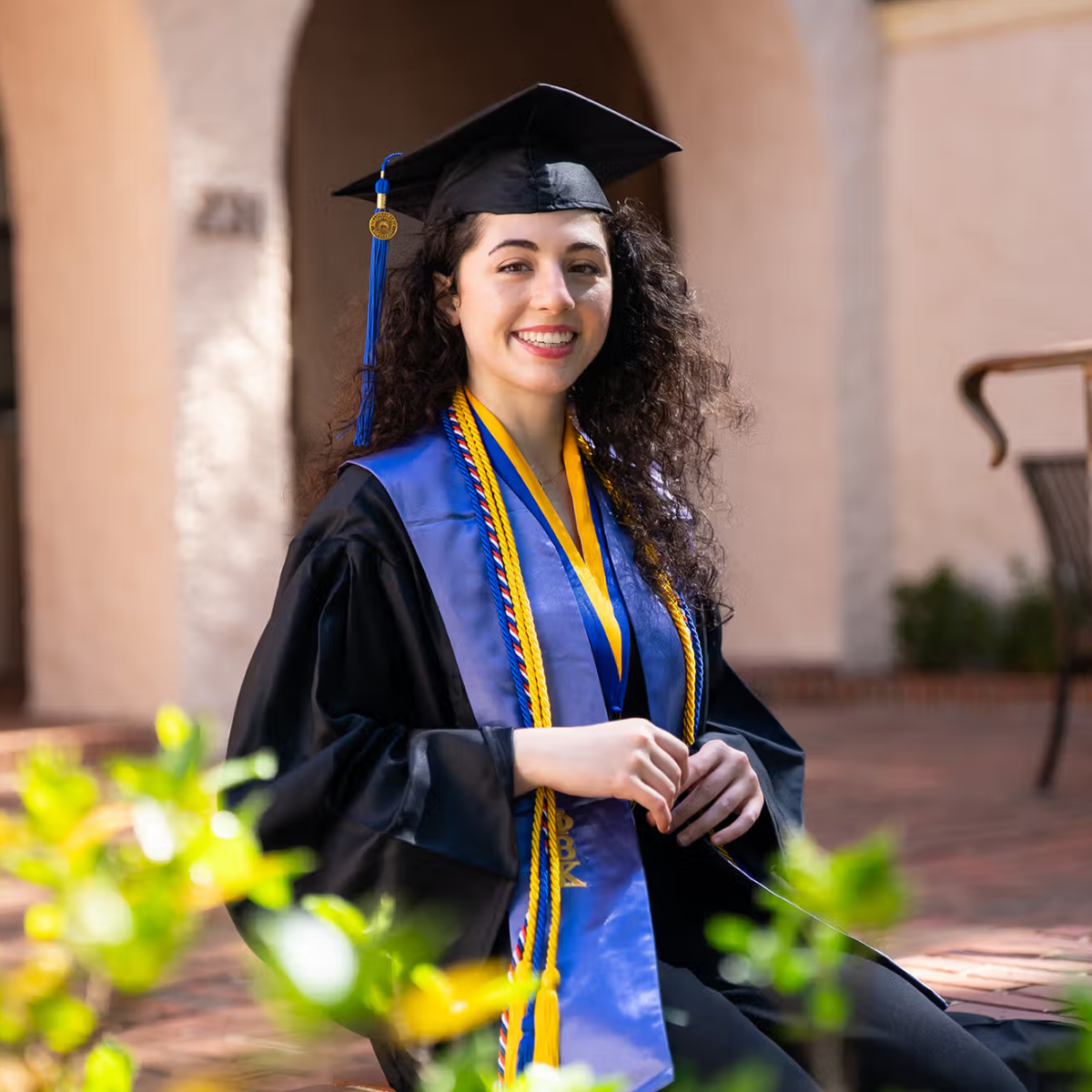 Abrielle, pictured on campus, smiling in her graduation regalia.