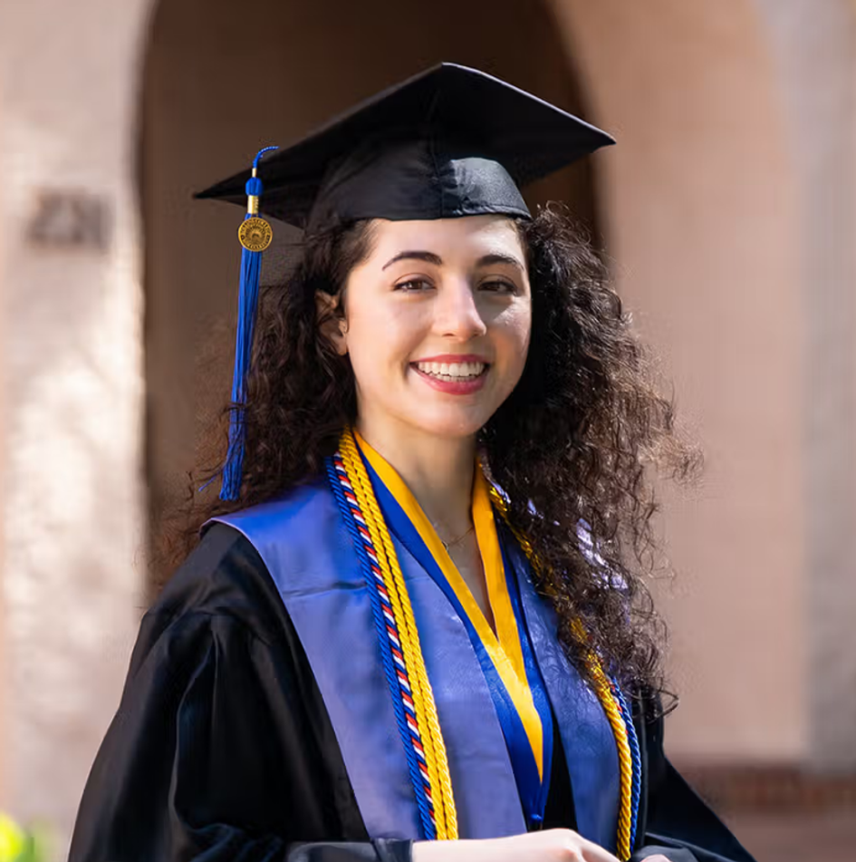 Abrielle, pictured on campus, smiling in her graduation regalia.