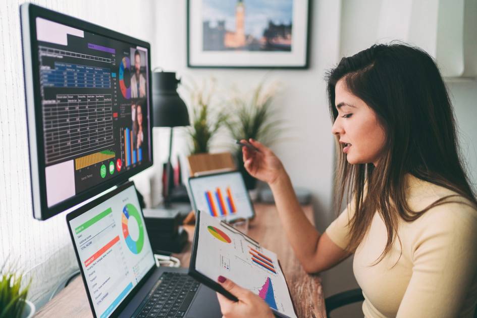 Professional analyzing financial charts during virtual meeting on multiple screens at desk