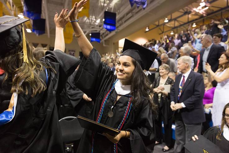 A graduate waves to her family in the crowd during commencement.