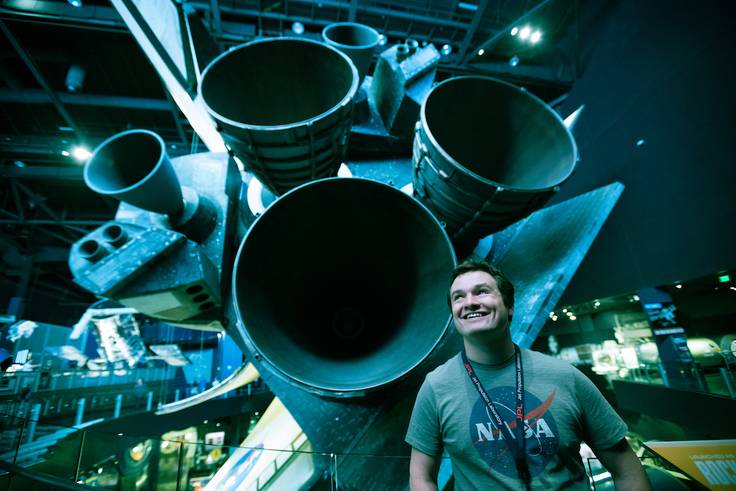 Rollins College computer science graduate, Michael Gutensohn ’18, poses in front of a rocket ship at the Kennedy Space Center. 