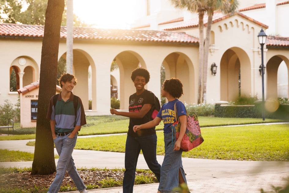 Three college students have a conversation as they walk across the Rollins College campus.