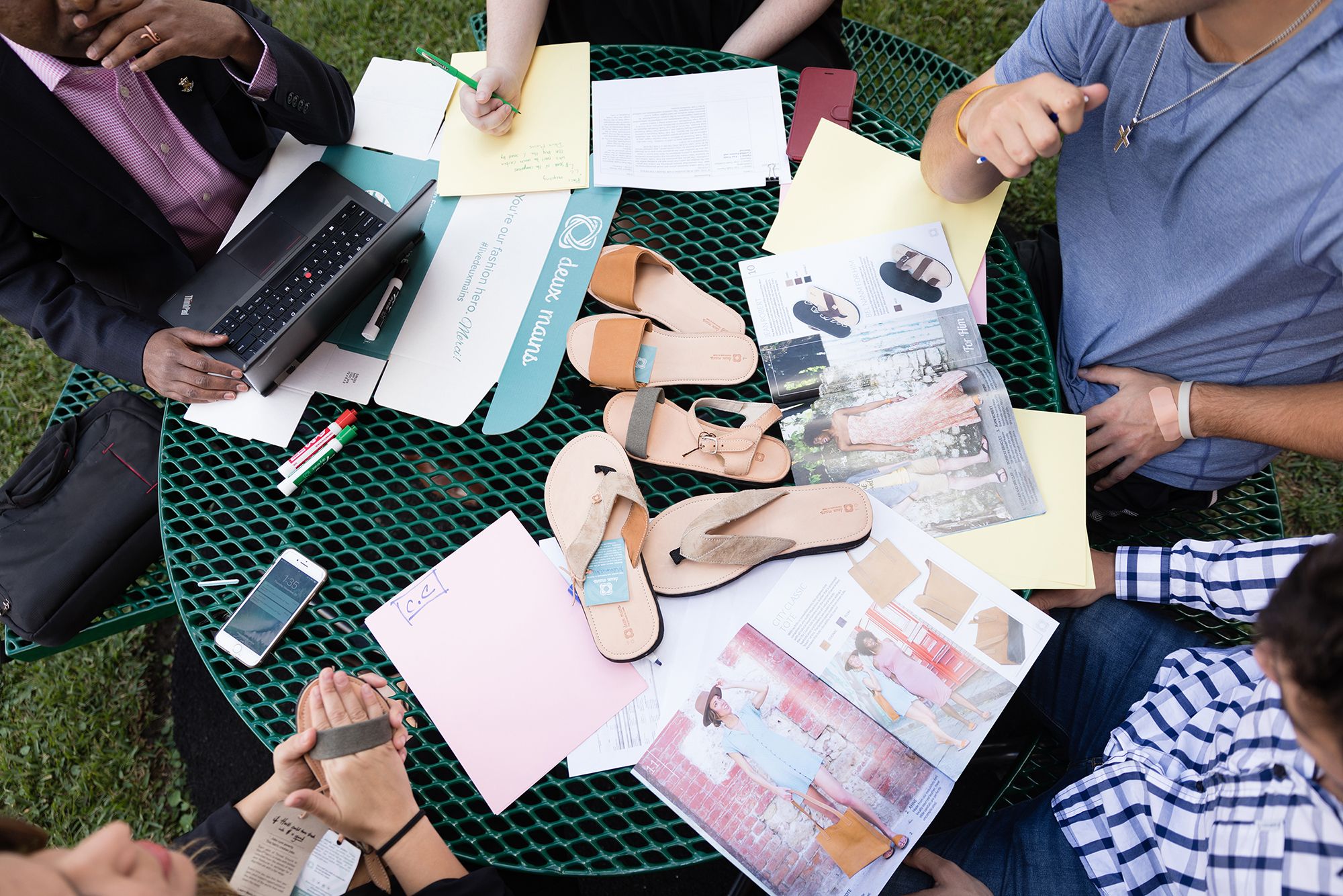 Deux Mains sandals and merchandise laid on a table surrounded by college students.