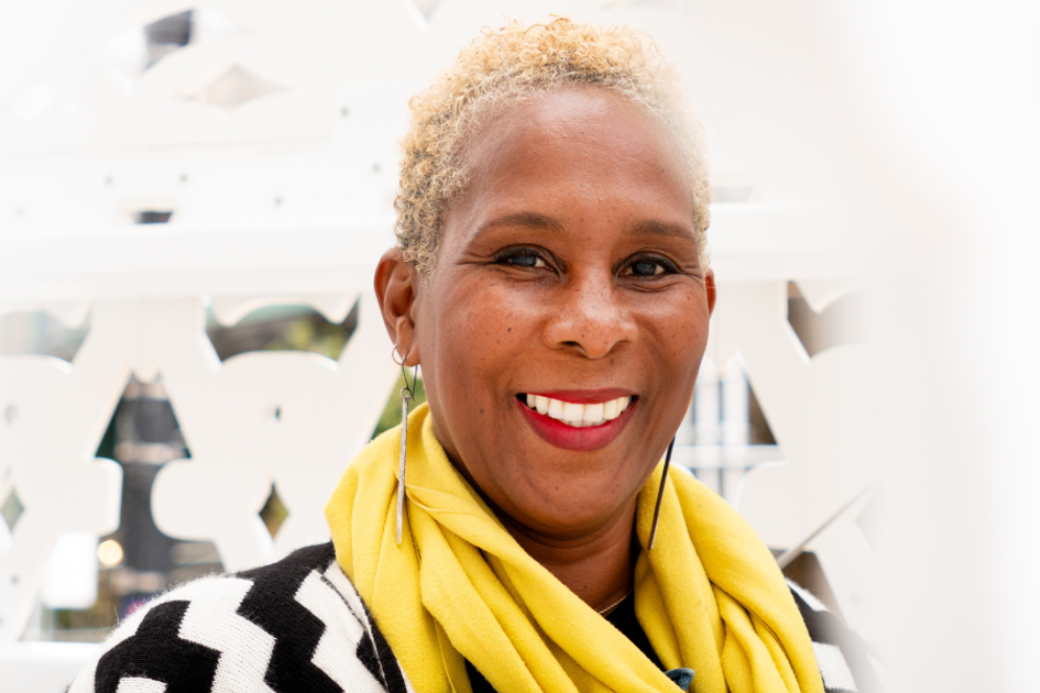 Smiling person wearing yellow scarf, posing against bright, patterned background.