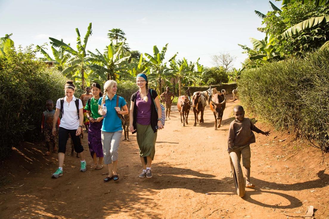 On the walk back from school, members of the Rollins group pass a village kid who plays a local favorite of pushing a tire with a stick. In the background, another village boy moves a herd of cows.