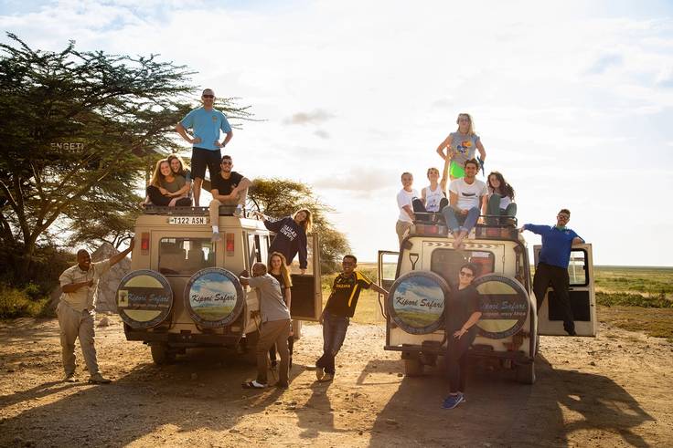 A group of students pose on a pair of jeeps during a safari in Serengeti National Park.