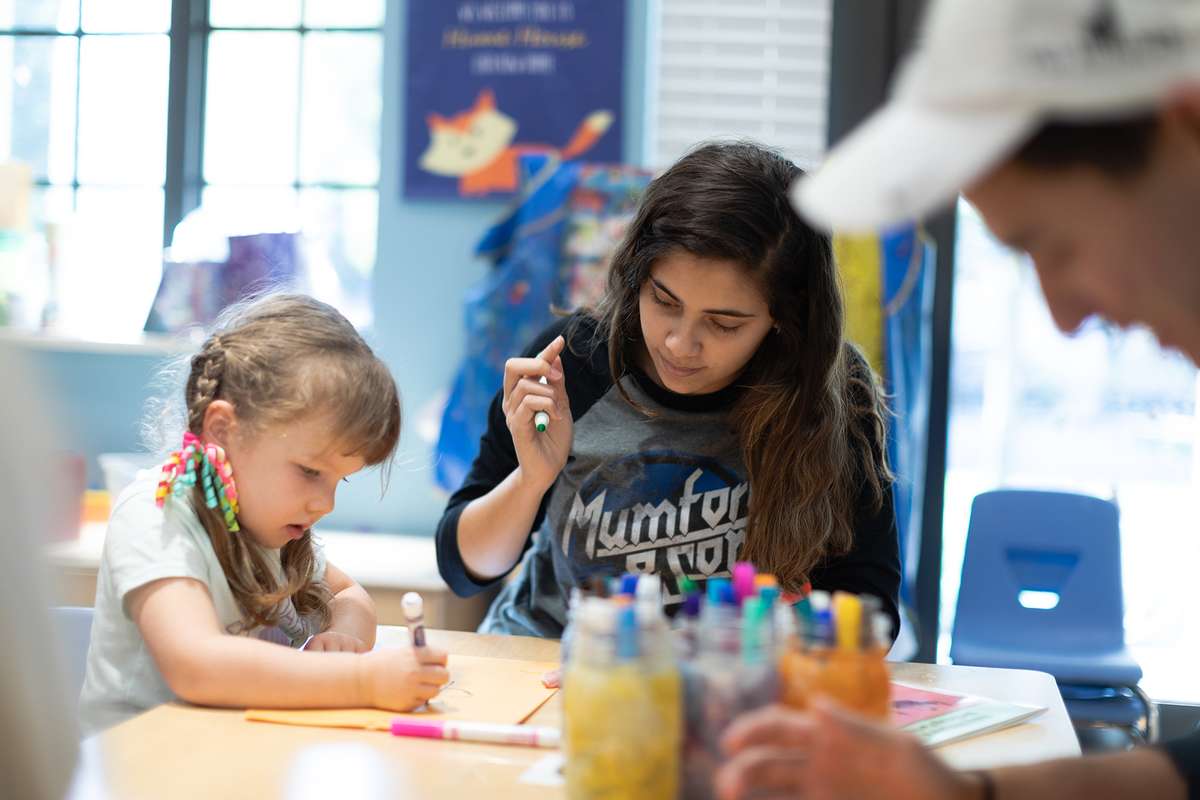 A college student and child coloring together with markers at a table.