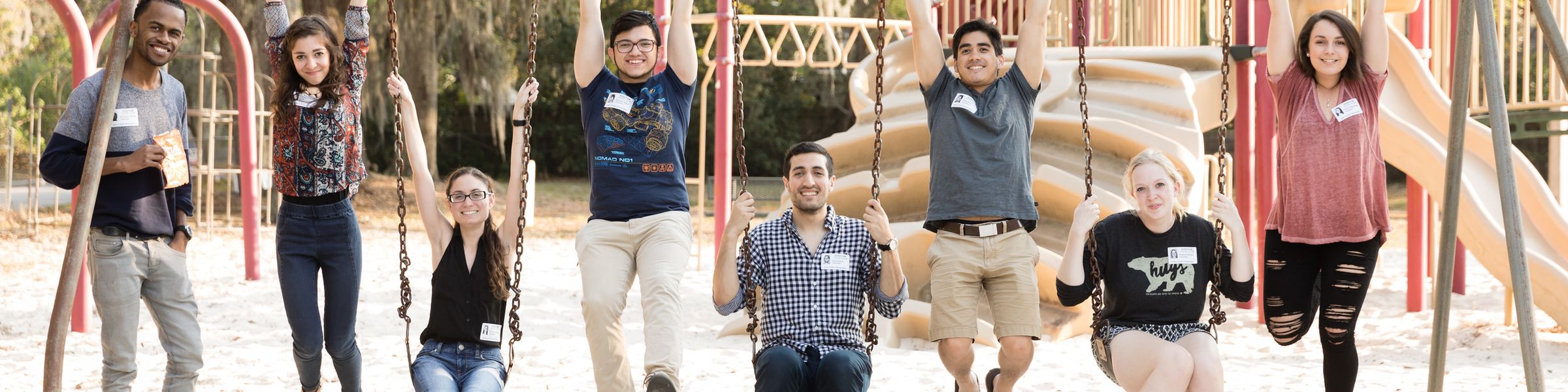 A playground with 8 alumni hanging and swinging on swingset