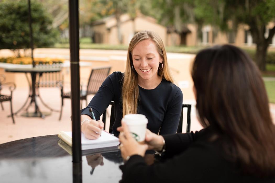 A student mentee takes notes while meeting with her alumni mentor.