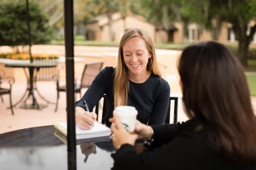 A student mentee takes notes while meeting with her alumni mentor.