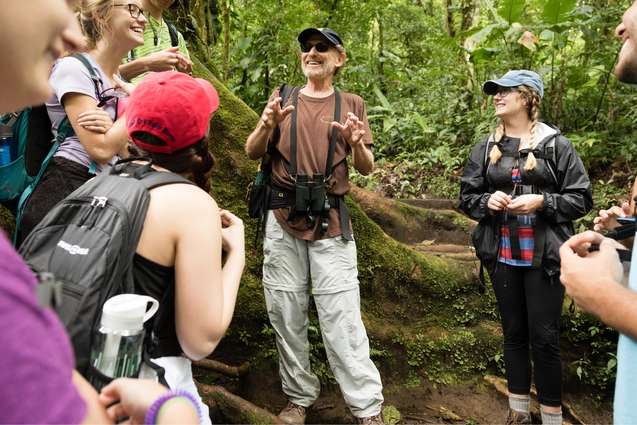 Ecology college professor addressing his class as they stand near a large tree in a Costa Rican rain forest.