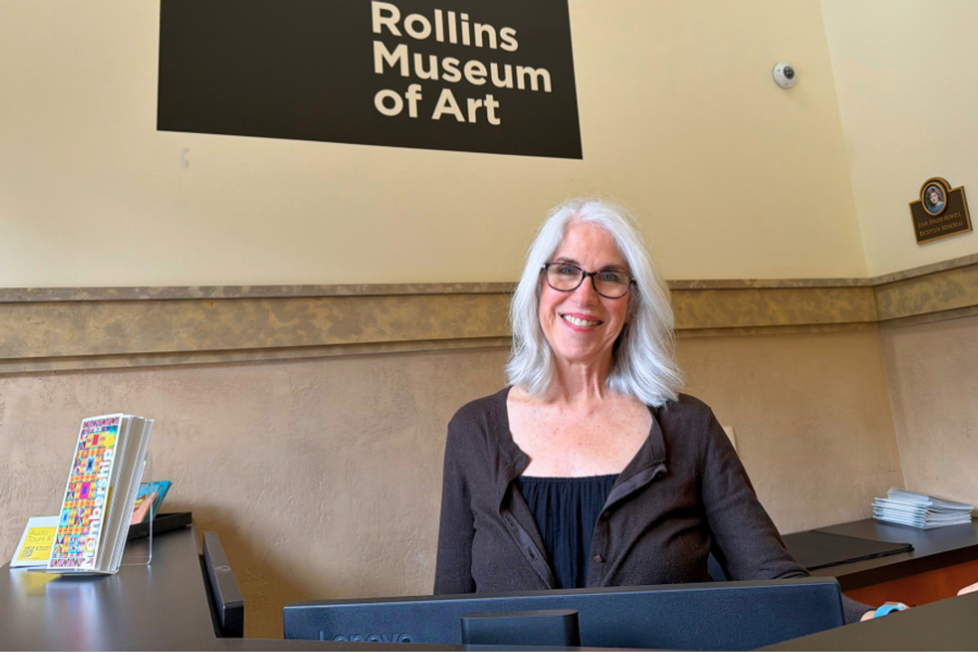 Woman smiles standing behind a desk at Rollins Museum of Art