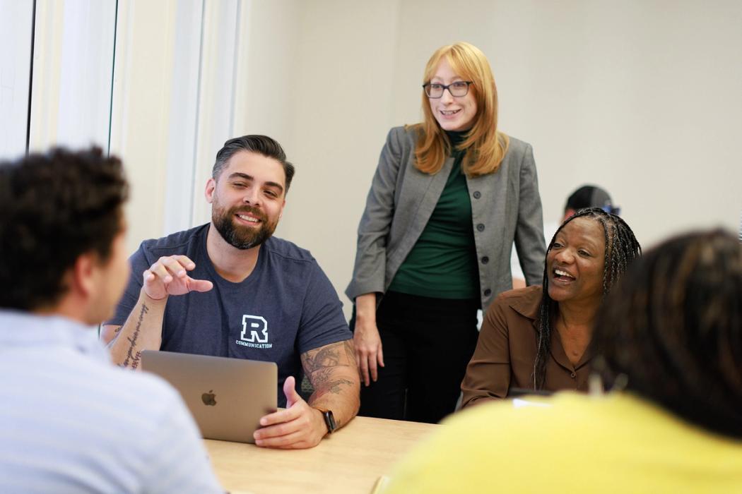 A professor chats with a small group of students during a communications class.