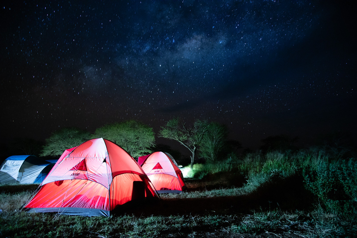 Three tents lit up in shades of red, green, and blue under a star-filled sky in Tanzania.