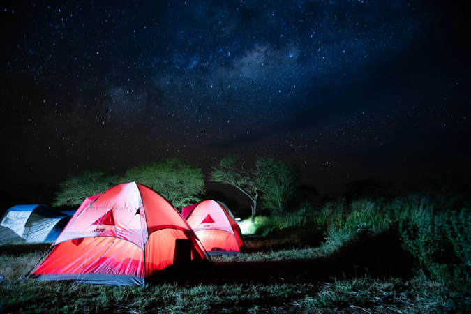 Three tents lit up in shades of red, green, and blue under a star-filled sky in Tanzania.