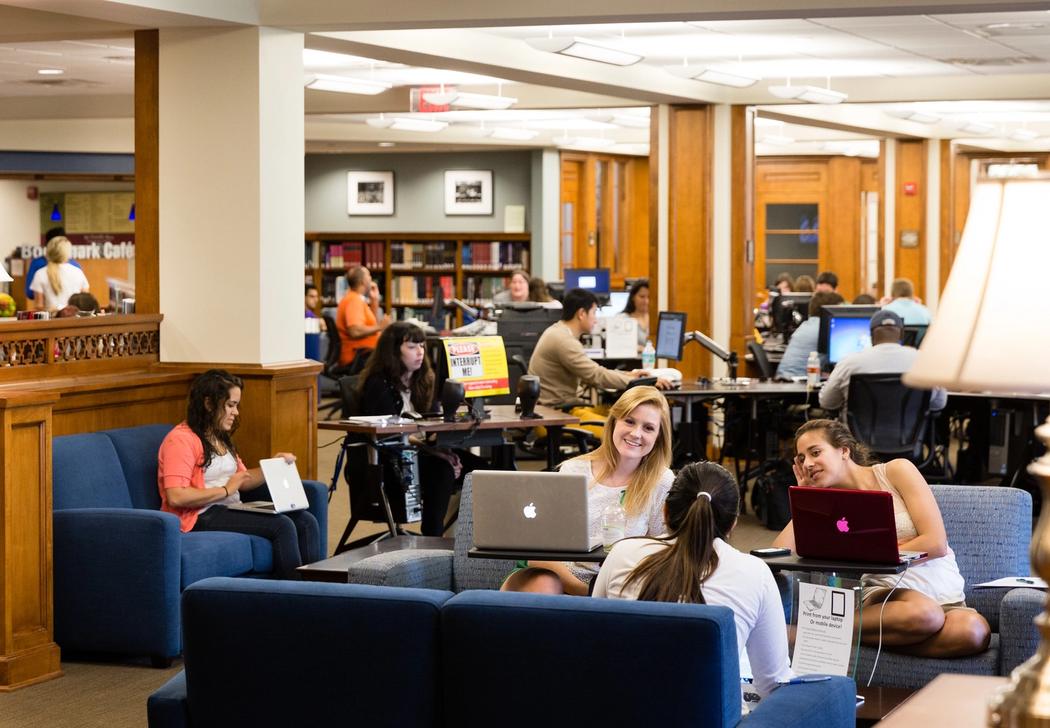 Students sitting in a lounge, reading books and using laptops.